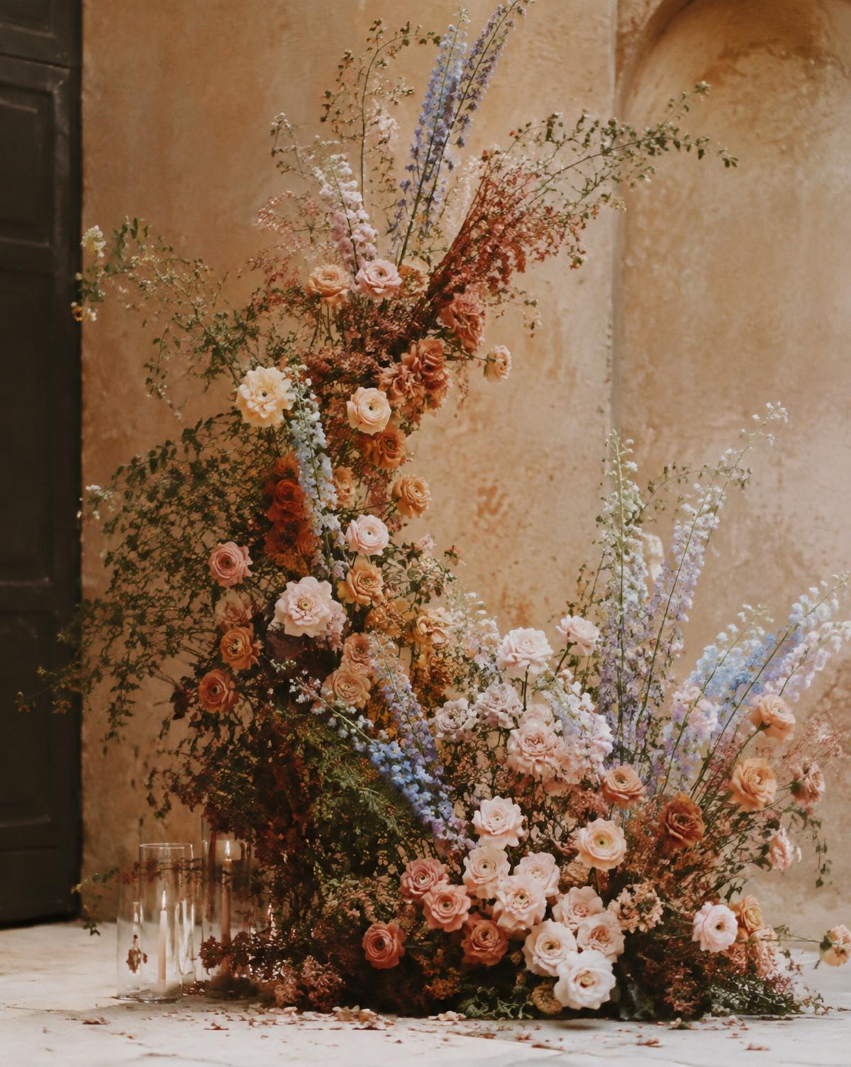 Sculptural terracotta and blush floral installation against a warm Italian stucco wall